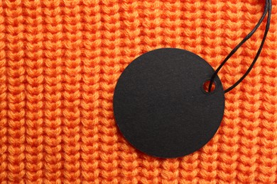 Circle shaped tag with space for text on orange knitted background, top view
