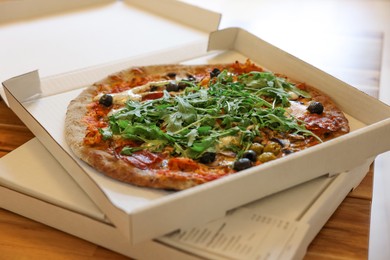 Delicious pizza with arugula, mushrooms and olives in box on wooden table, closeup