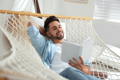 Young man reading book in hammock at home