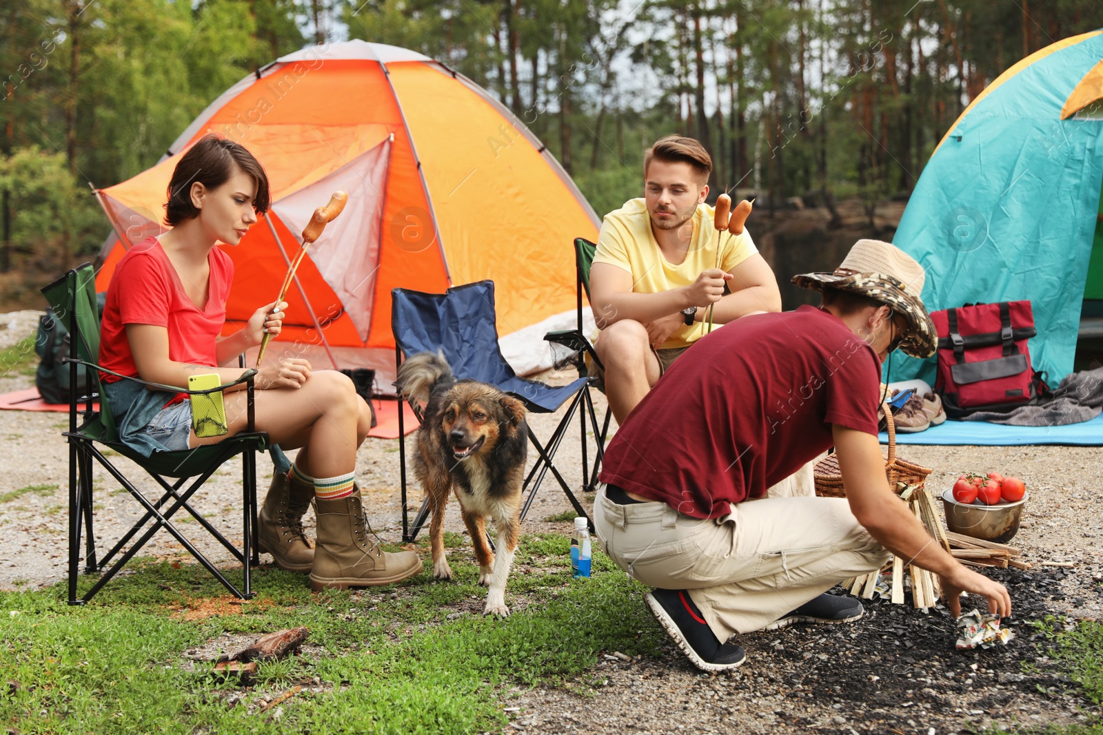 Photo of Young people having lunch with sausages near camping tents outdoors