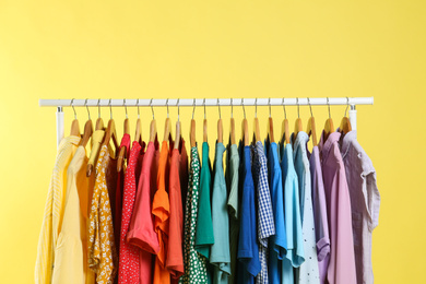 Photo of Bright clothes hanging on rack against yellow background. Rainbow colors