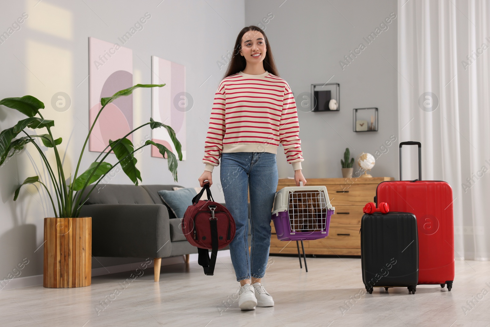 Photo of Travel with pet. Smiling woman holding carrier with dog and bag at home