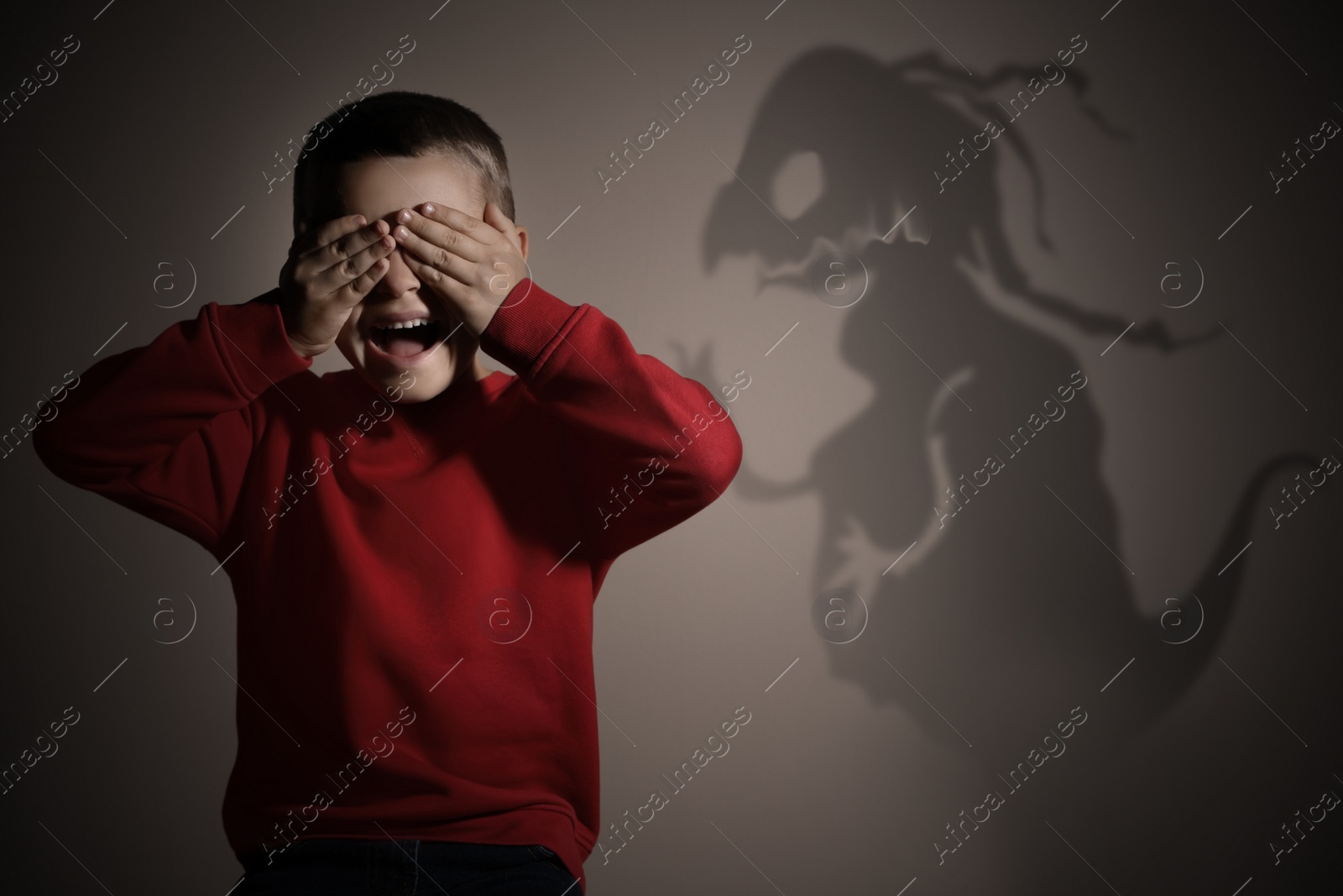 Image of Shadow of monster and scared little boy on beige background