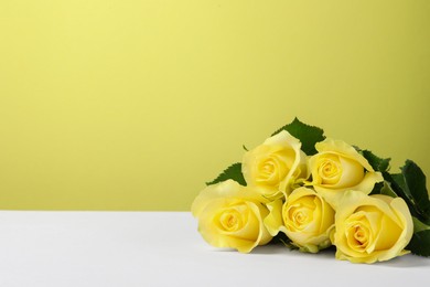 Beautiful fresh roses on white table against yellow background. Space for text