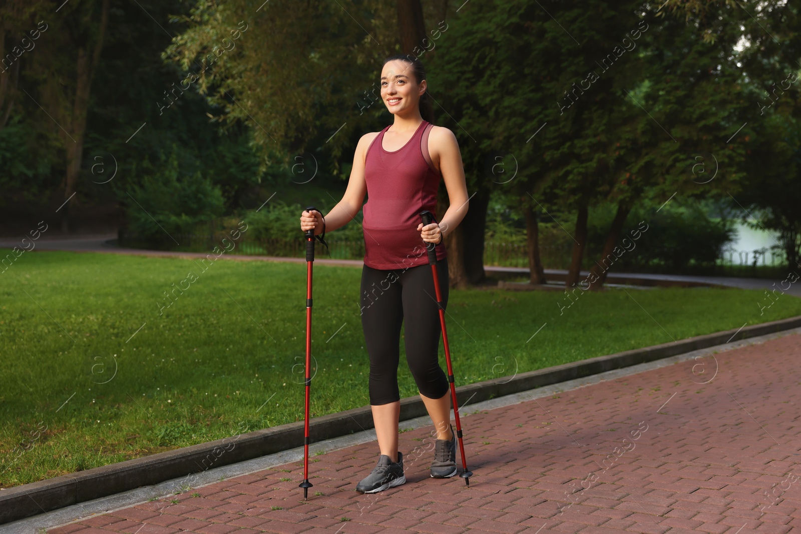 Photo of Pregnant woman practicing Nordic walking with poles outdoors