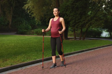 Photo of Pregnant woman practicing Nordic walking with poles outdoors