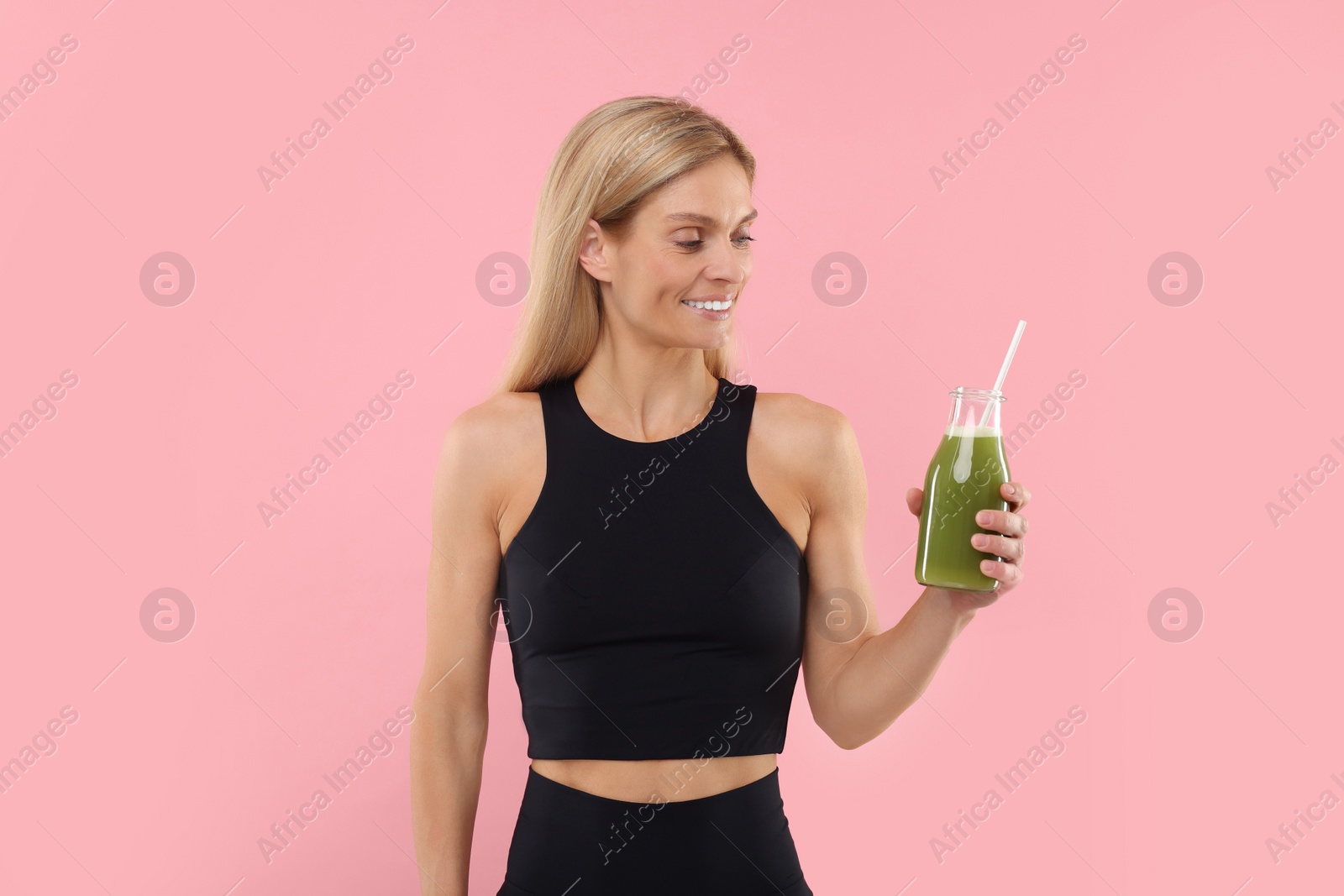 Photo of Happy woman with glass bottle of fresh celery juice on pink background