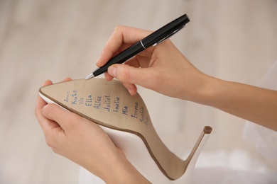 Photo of Young bride writing her single friends names on shoe indoors, closeup. Wedding superstition