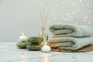 Spa composition. Herbal massage bags, stones, reed air freshener and burning candles on white marble table, space for text