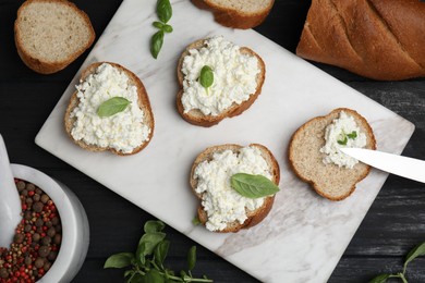 Photo of Bread with cottage cheese and basil on black wooden table, flat lay