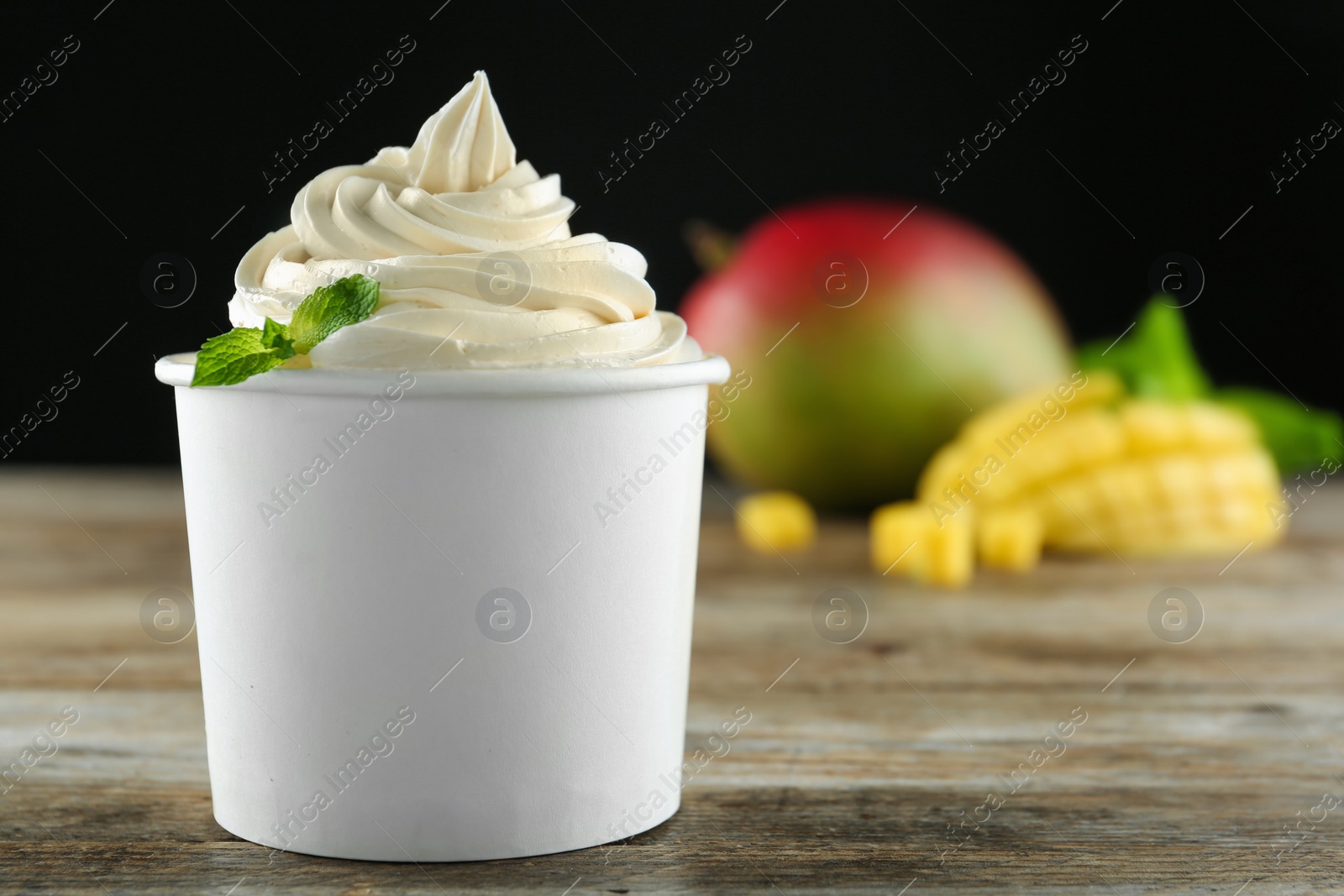 Photo of Cup with tasty frozen yogurt and mango on wooden table. Space for text