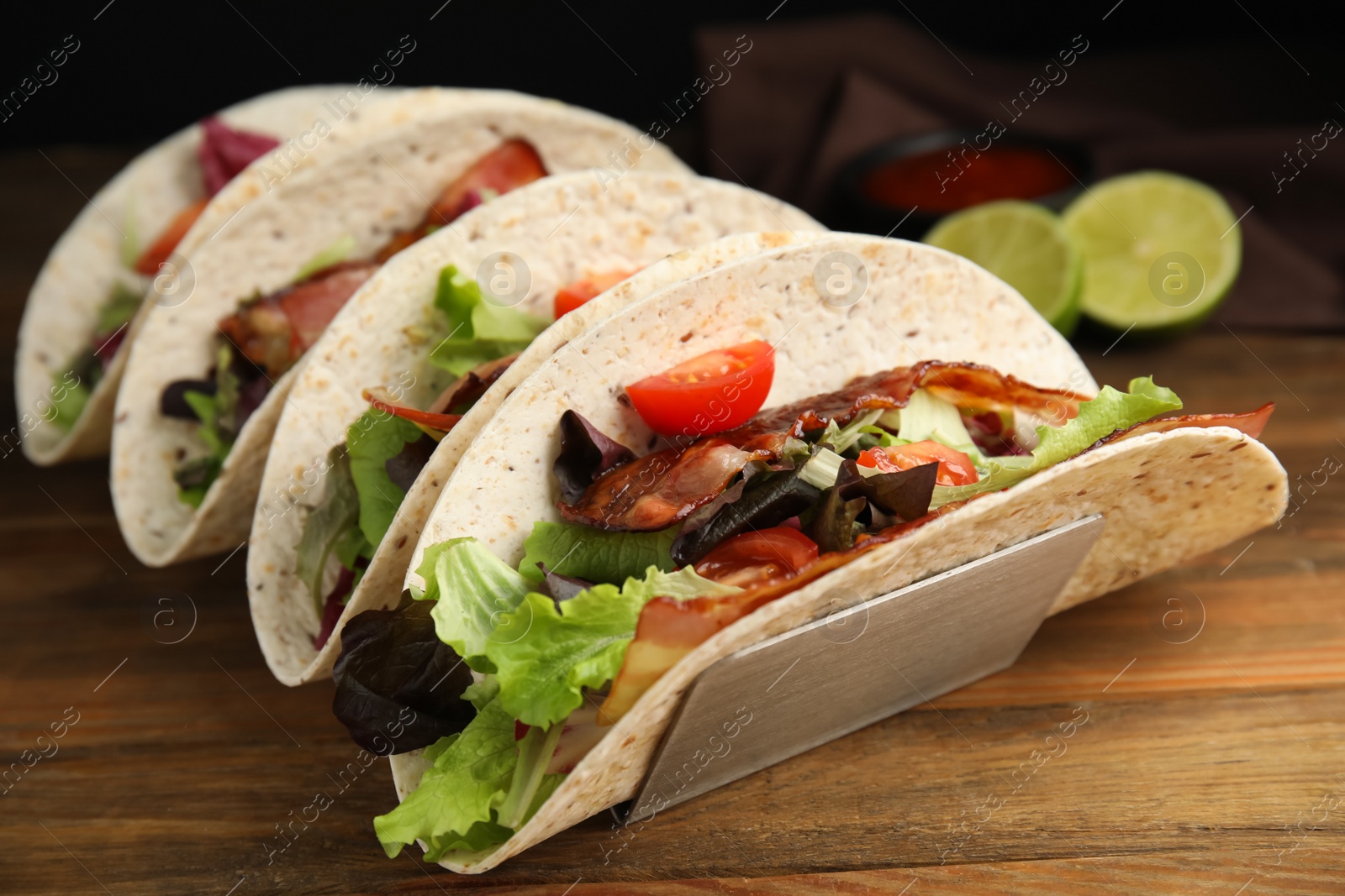 Photo of Delicious tacos with fried bacon on wooden table, closeup