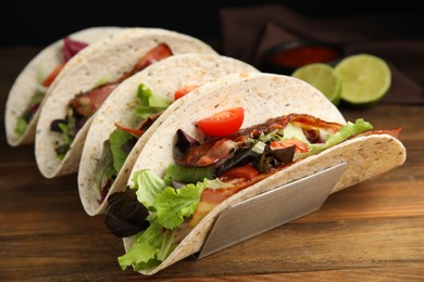 Photo of Delicious tacos with fried bacon on wooden table, closeup