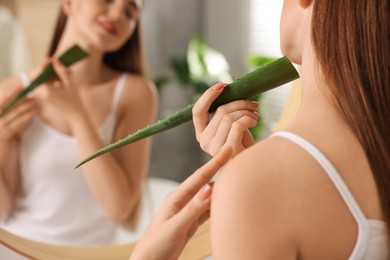Photo of Young woman applying aloe gel from leaf onto her neck near mirror in bathroom, closeup