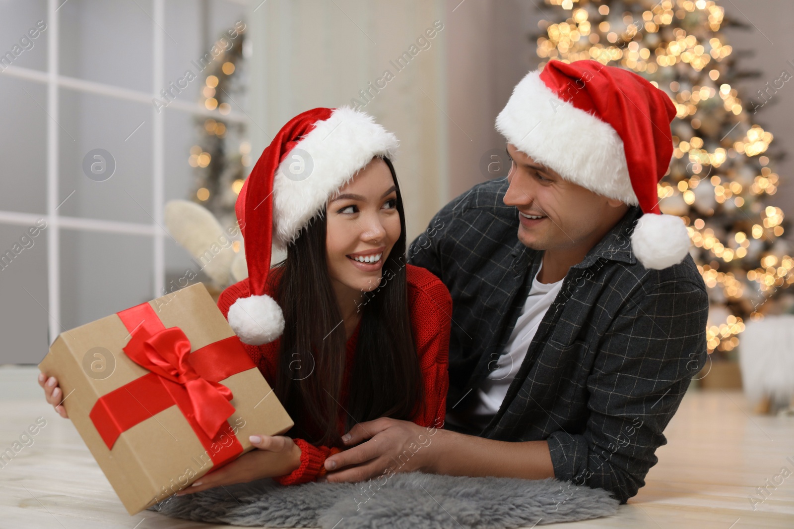 Photo of Happy young couple in Santa hats with Christmas gift at home