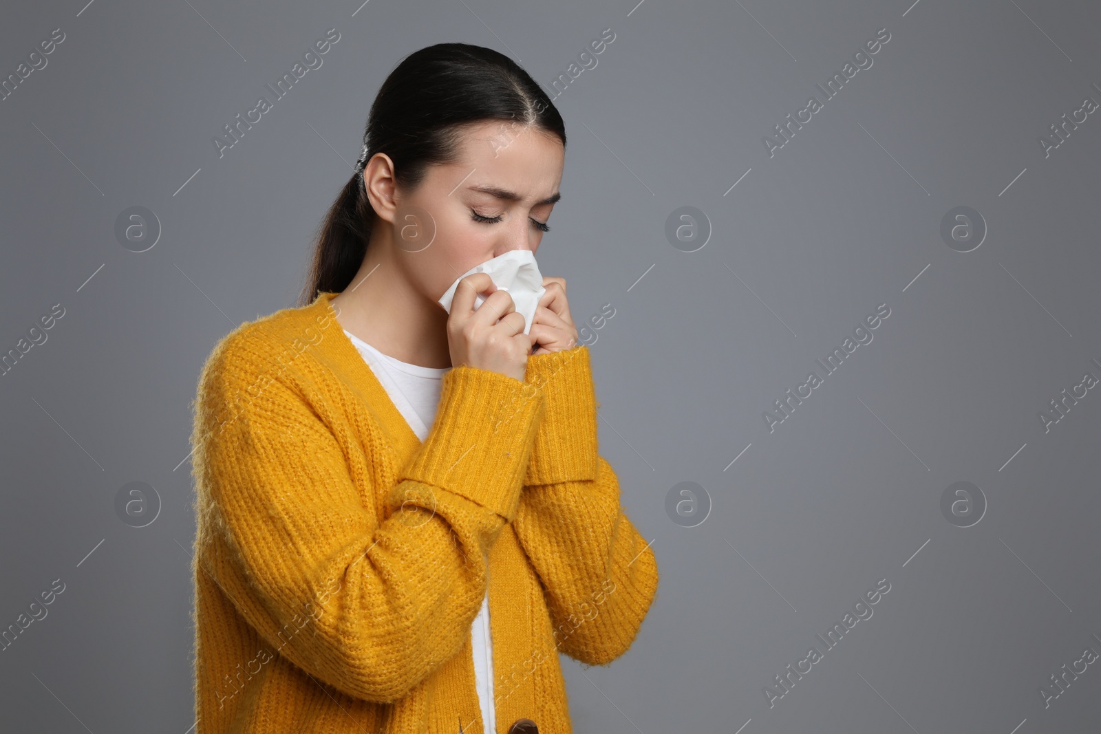 Photo of Young woman blowing nose in tissue on grey background, space for text. Cold symptoms