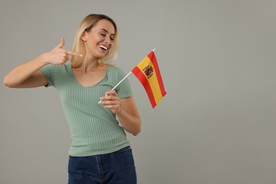 Happy woman pointing at flag of Spain on grey background, space for text