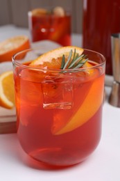 Photo of Aperol spritz cocktail, ice cubes, rosemary and orange slices in glass on white wooden table, closeup