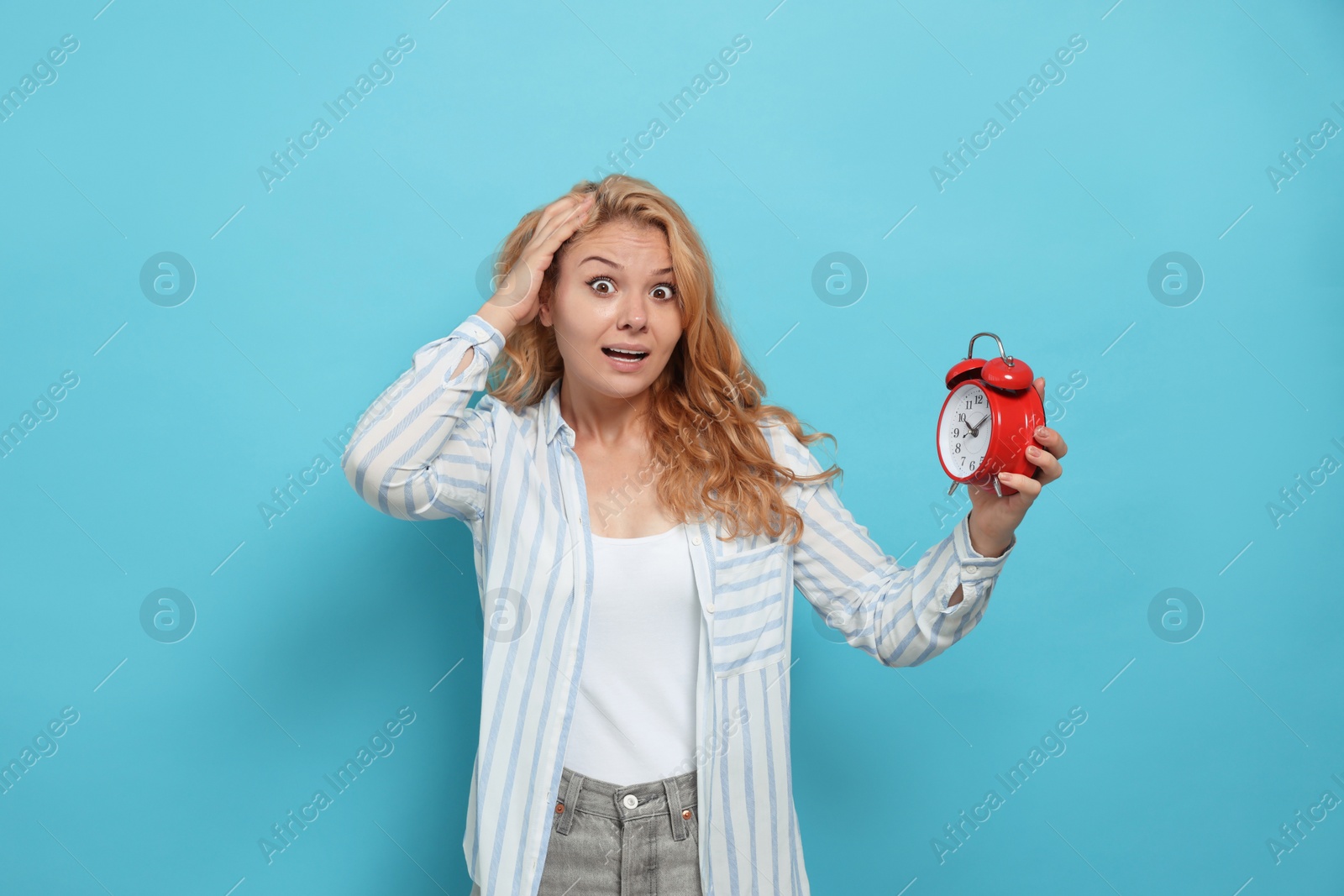 Photo of Emotional woman with alarm clock in turmoil over being late on light blue background