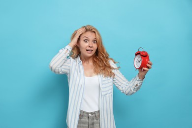 Photo of Emotional woman with alarm clock in turmoil over being late on light blue background