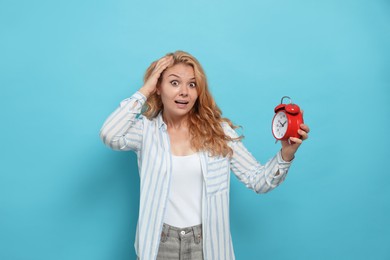 Emotional woman with alarm clock in turmoil over being late on light blue background