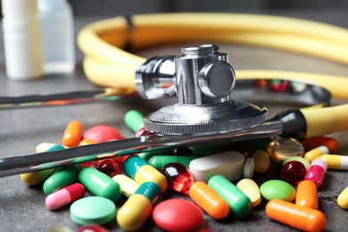 Stethoscope and pills on grey table, closeup. Medical objects