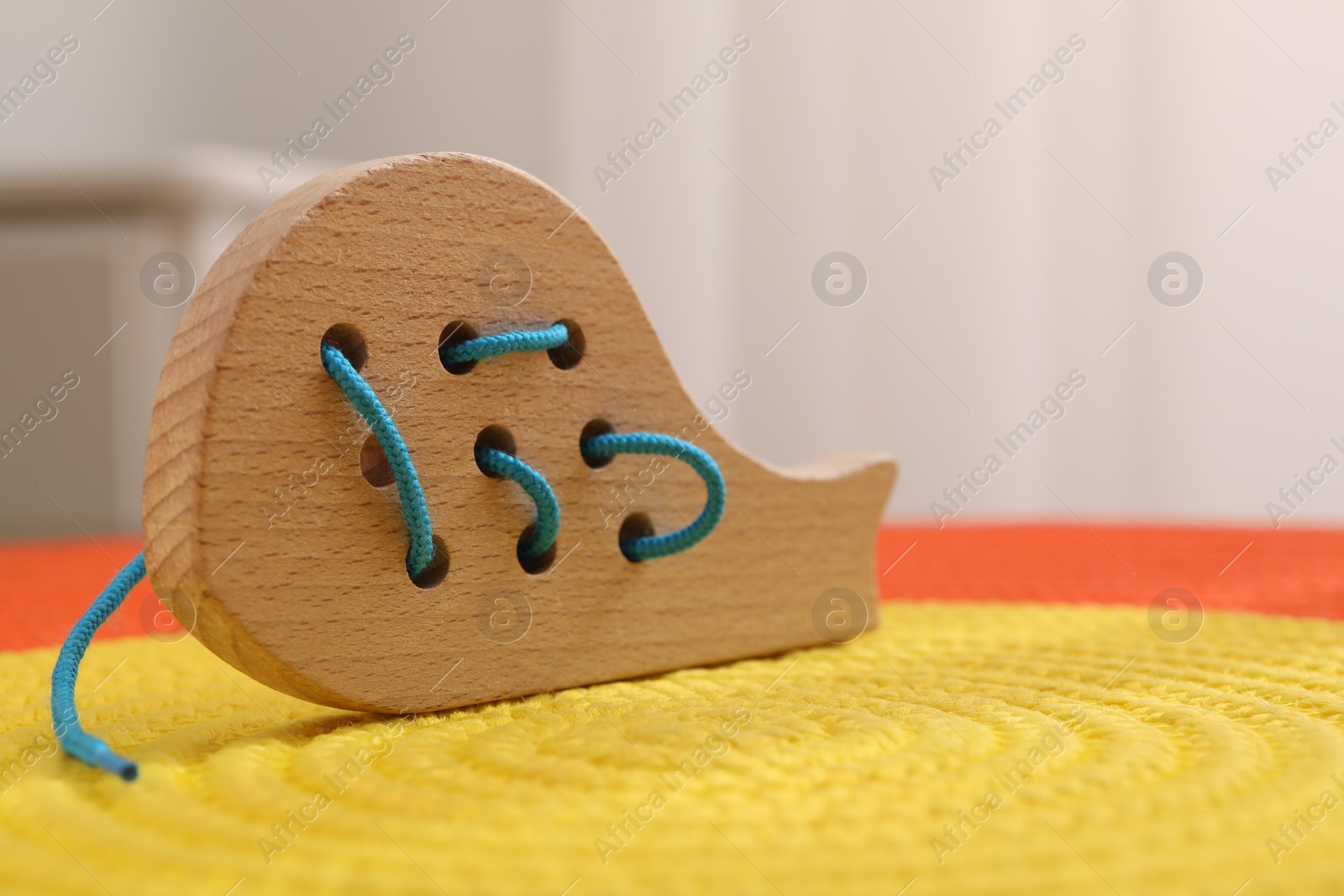 Photo of Motor skills development. Wooden lacing toy on color mat against light background, closeup. Space for text