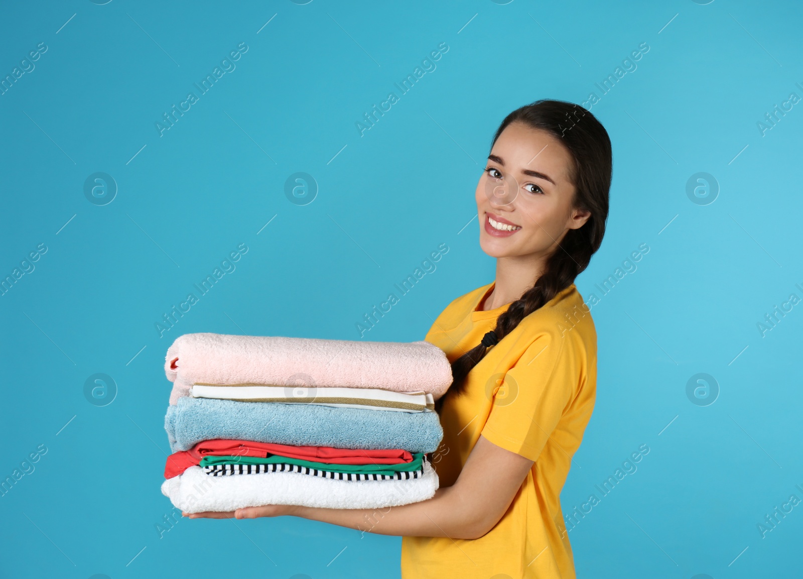 Photo of Happy young woman holding clean laundry on color background