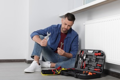 Photo of Man choosing wrench near box with tools indoors