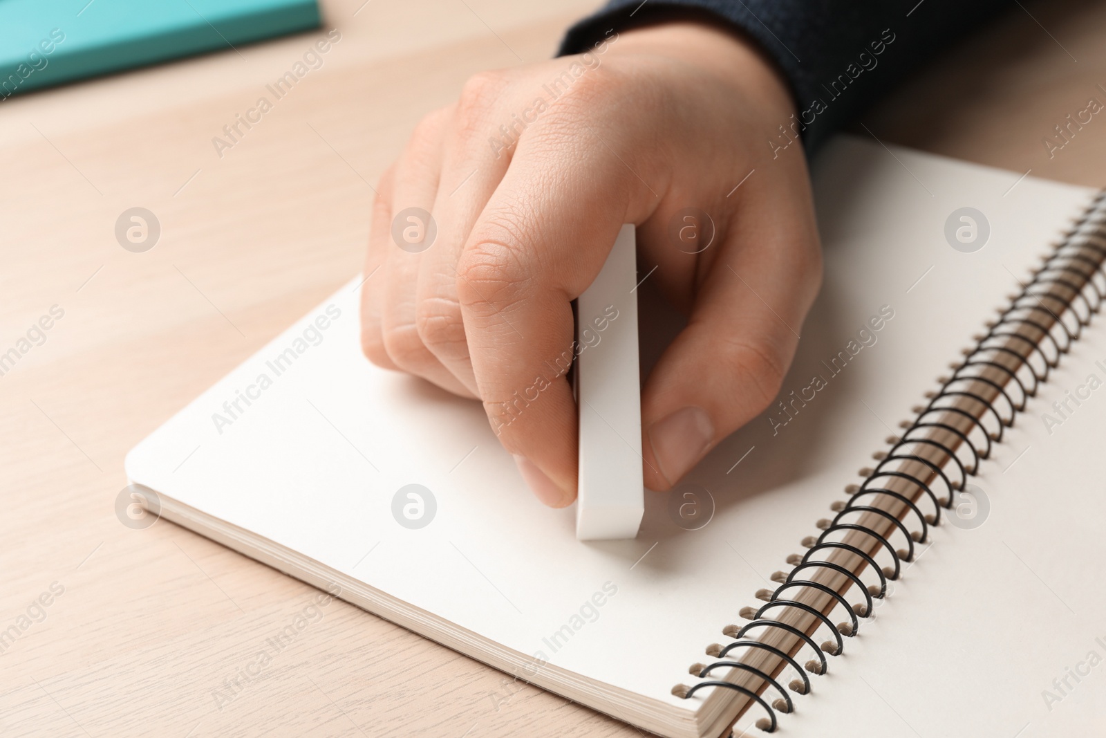 Photo of Man erasing something in notebook at wooden table, closeup