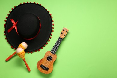 Photo of Mexican sombrero hat, maracas and guitar on green background, flat lay. Space for text