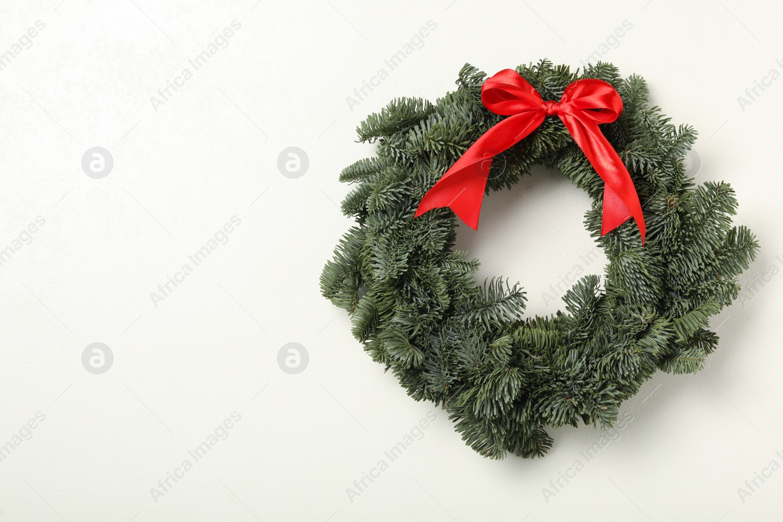 Photo of Christmas wreath made of fir tree branches with red ribbon on white background, space for text