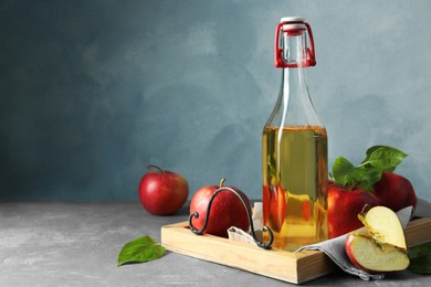Photo of Bottle of delicious cider and apples with green leaves on gray table, space for text