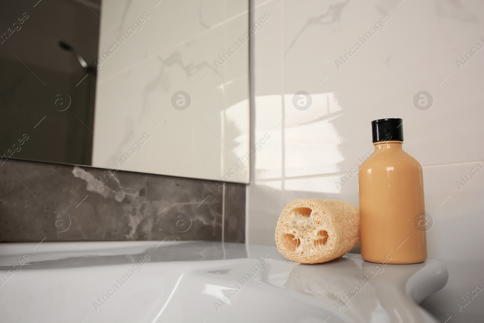 Photo of Natural loofah sponge and shower gel bottle on washbasin in bathroom, space for text