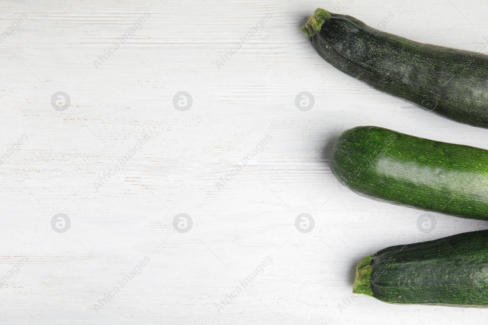 Photo of Fresh ripe green zucchinis on white wooden table, flat lay. Space for text