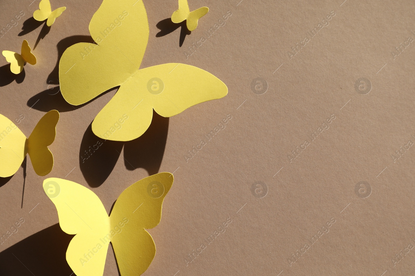 Photo of Yellow paper butterflies on light brown background, top view. Space for text