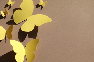 Yellow paper butterflies on light brown background, top view. Space for text