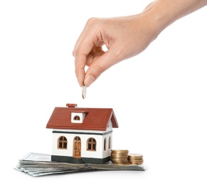 Woman putting coin into house model on white background