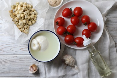 Delicious burrata cheese served with croutons and tomatoes on white wooden table, flat lay