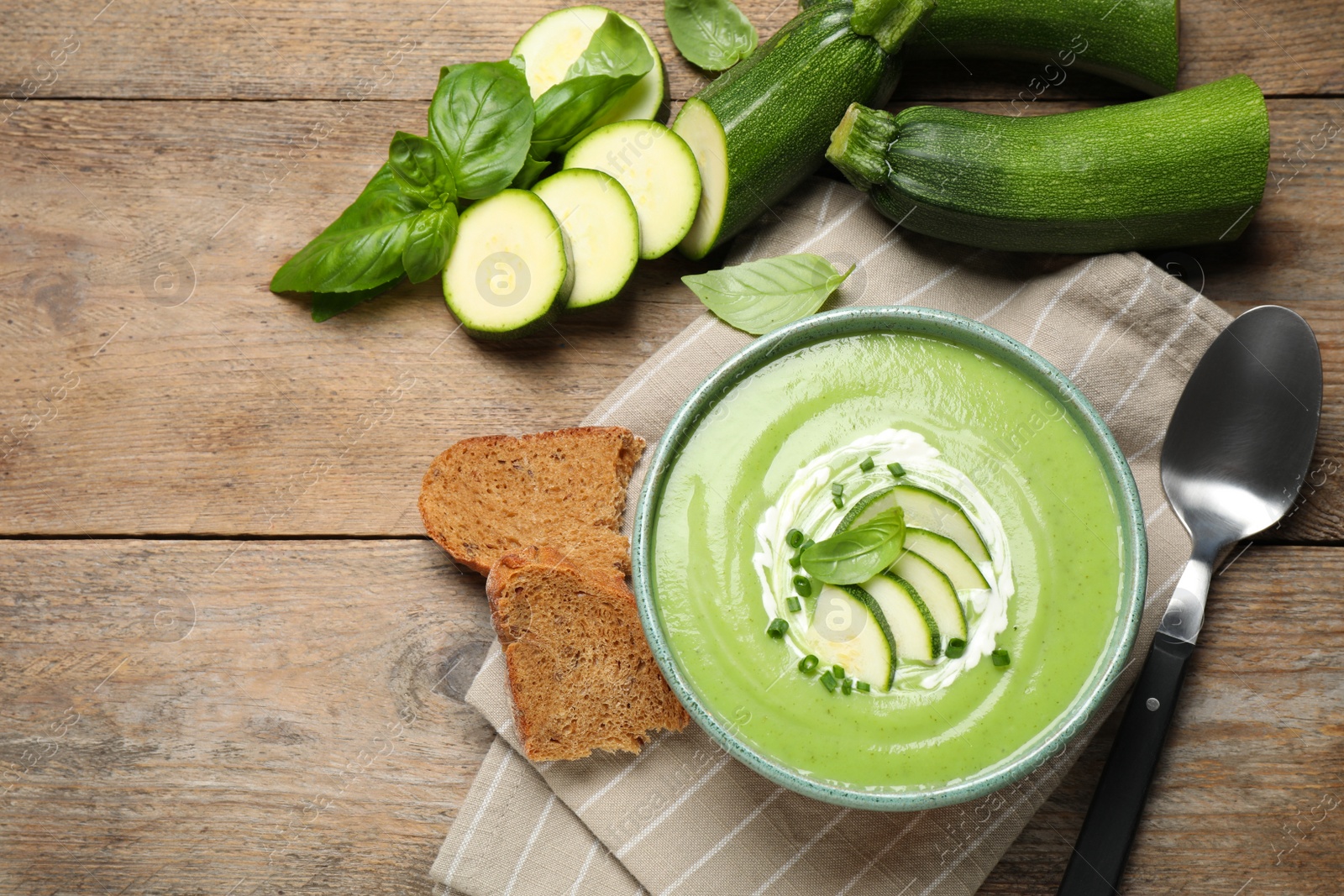Photo of Tasty homemade zucchini cream soup served on wooden table, flat lay