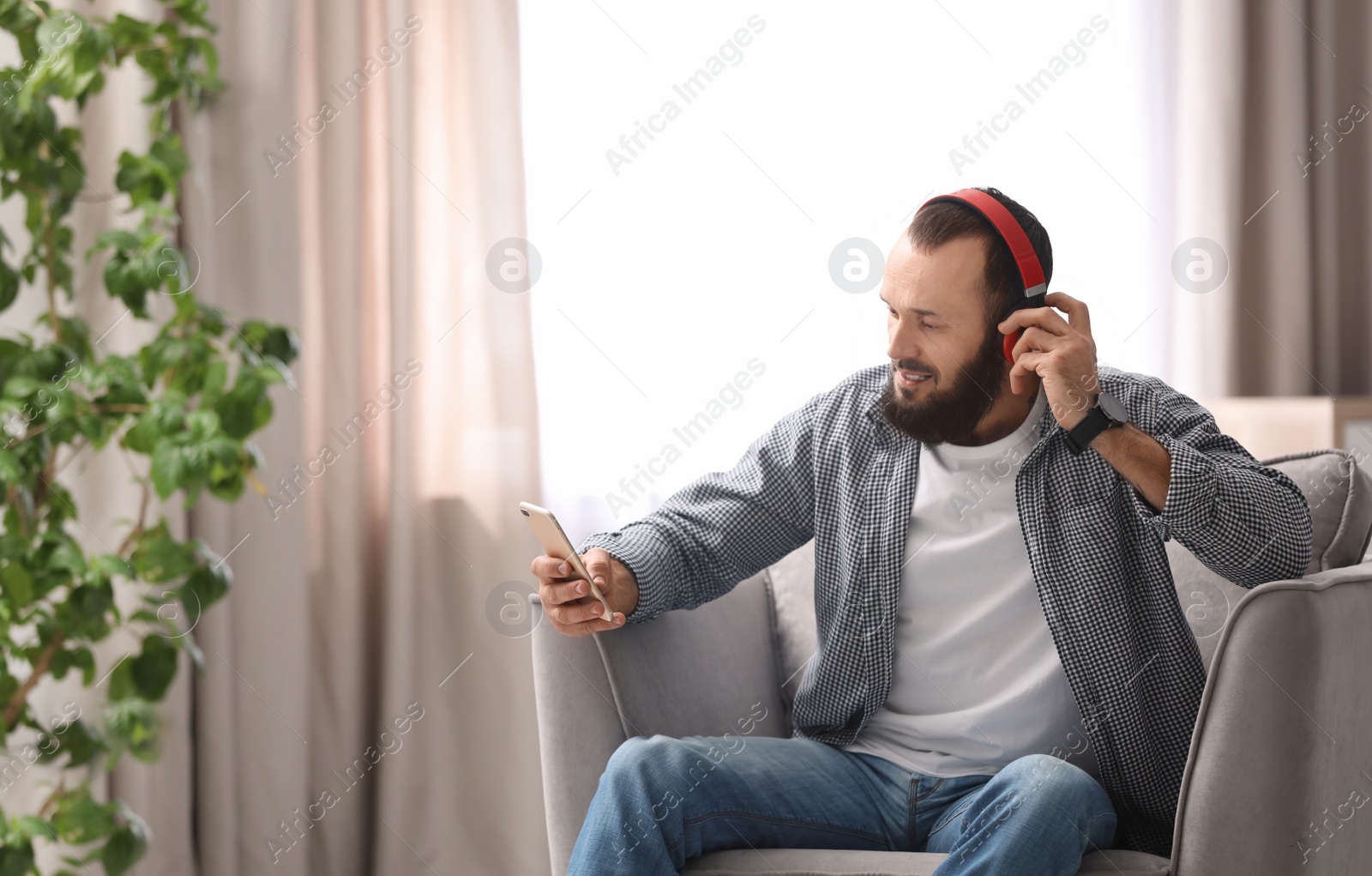 Photo of Mature man with headphones and mobile device resting in armchair at home