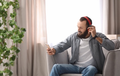 Photo of Mature man with headphones and mobile device resting in armchair at home