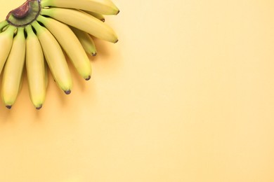 Bunch of ripe baby bananas on light orange background, top view. Space for text