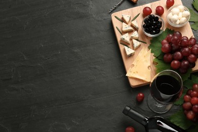 Tasty red wine and snacks on black table, flat lay. Space for text