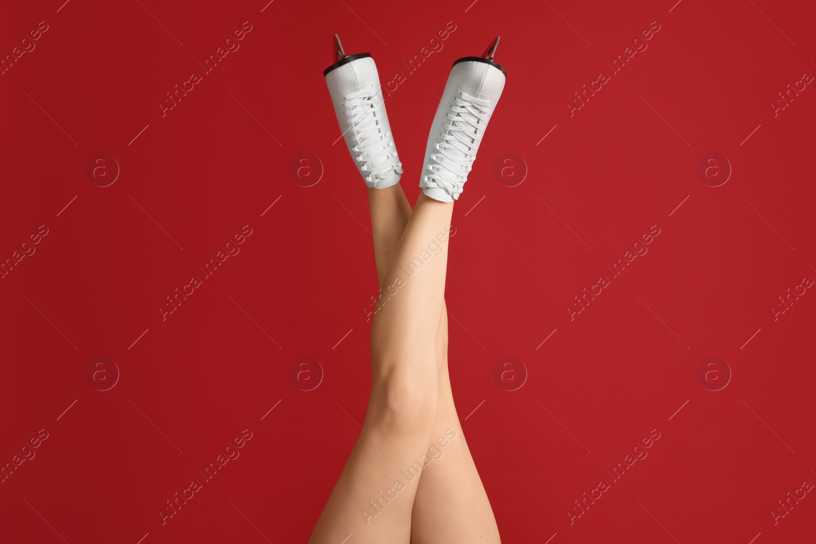 Photo of Woman in elegant white ice skates on red background, closeup of legs