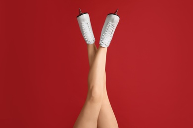 Photo of Woman in elegant white ice skates on red background, closeup of legs