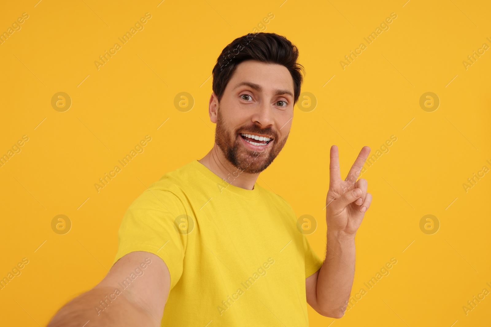 Photo of Smiling man taking selfie and showing peace sign on yellow background