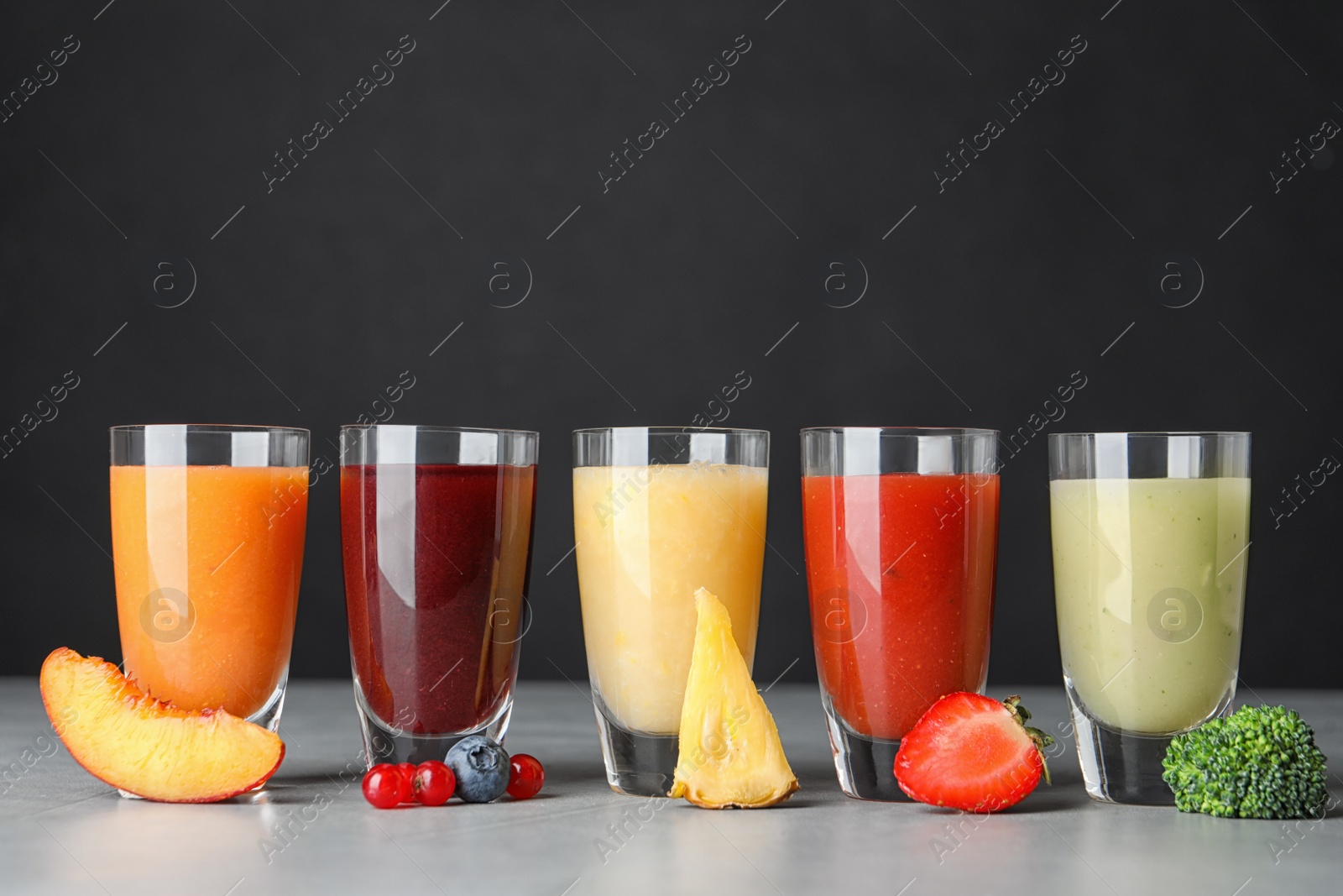 Photo of Delicious juices and fresh ingredients on grey table against black background