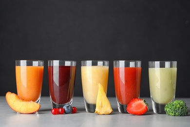 Photo of Delicious juices and fresh ingredients on grey table against black background