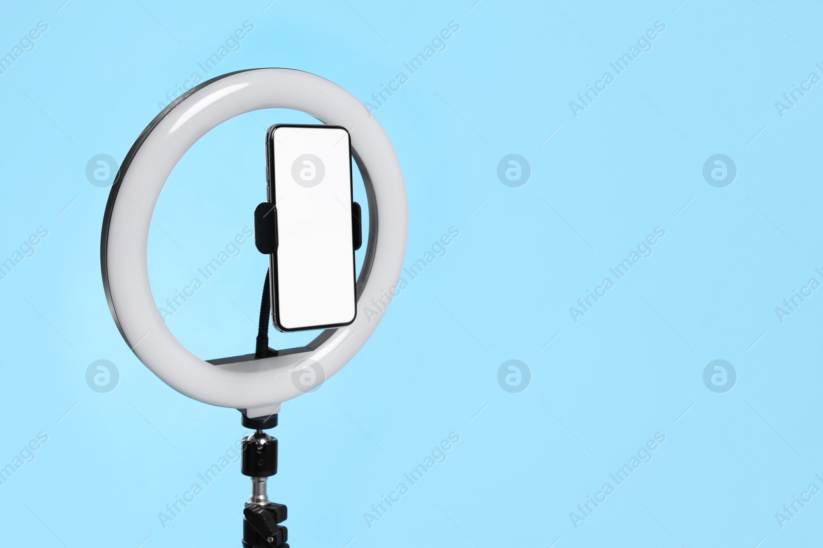 Photo of Modern tripod with ring light and smartphone on light blue background. Space for text